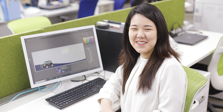 デザインした画像の前でほほ笑む新卒総合職女性Hさんの写真