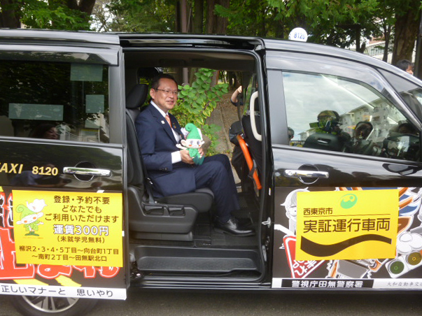 大和交通保谷のセレナ車両に乗り込む池澤隆史西東京市市長と、西東京市マスコットキャラクター「いこいーな」のぬいぐるみ