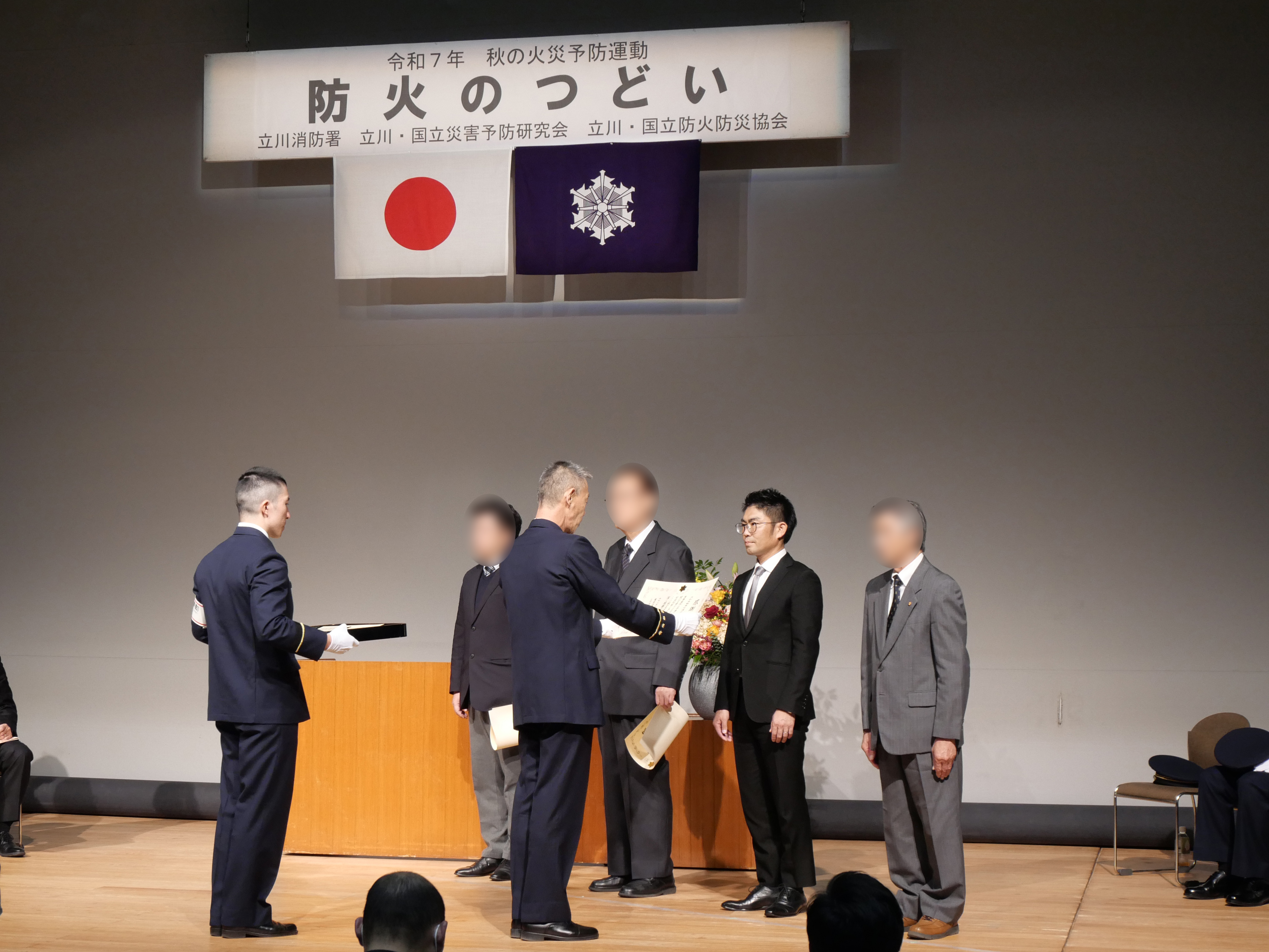 『防火のつどい』第一部　火災予防業務協力功労者表彰式の写真。大和自動車交通立川㈱の澤田社長が登壇し、感謝状を受け取っている様子。
