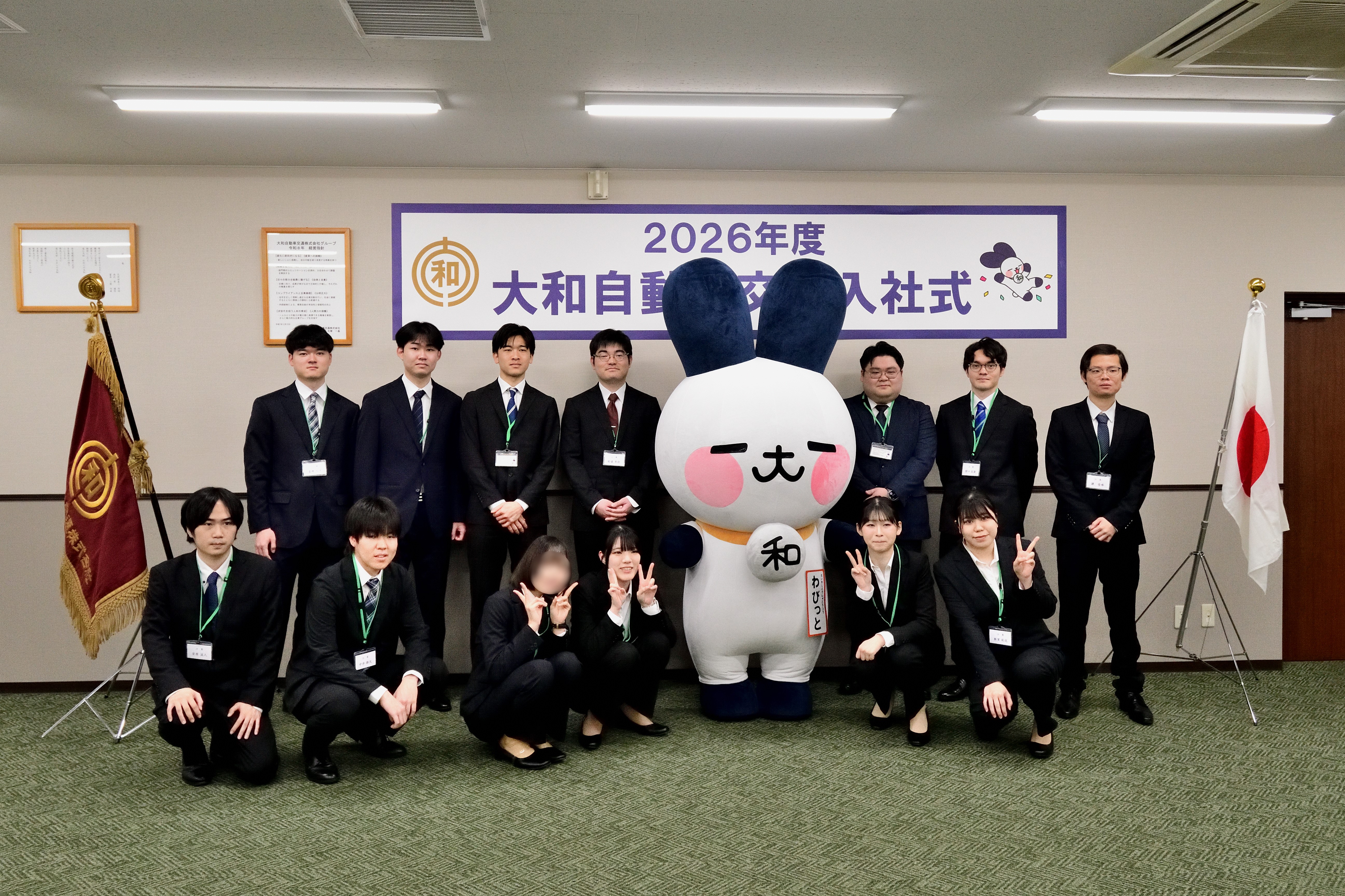 2026年度入社式でマスコットキャラクター「わびっと」と記念撮影する新入社員